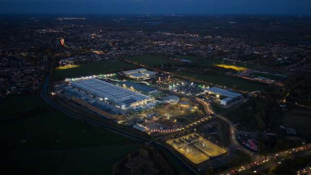 An aerial view of a well-lit data center near a city at dusk, featuring warehouses and sports fields.