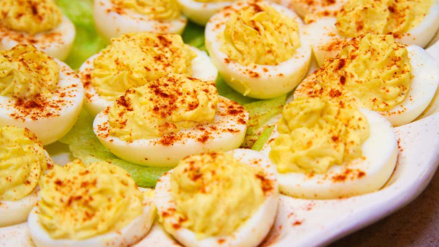 A platter of deviled eggs garnished with paprika on a bed of lettuce.