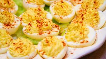 A platter of deviled eggs garnished with paprika on a bed of lettuce.