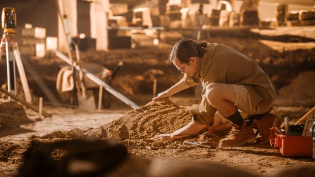 A person in work attire carefully examines items during an archeological dig.