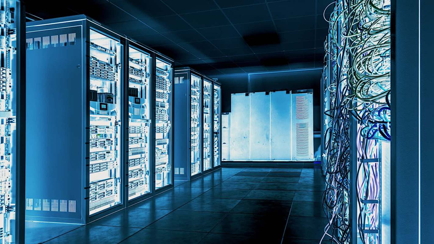 A dimly lit data center filled with server racks and tangled cables against a blue-toned backdrop.