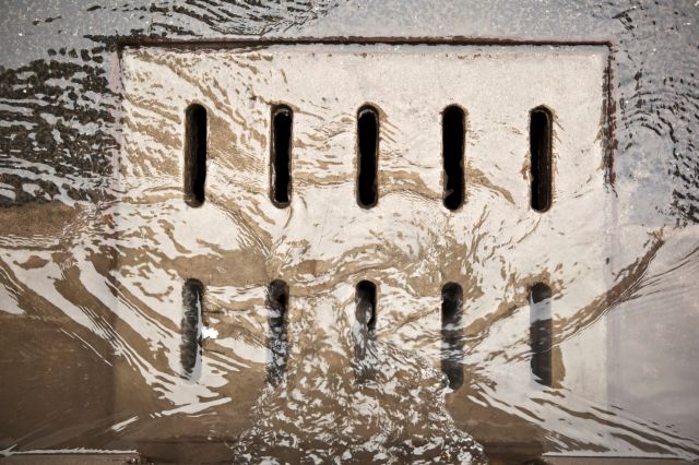 A close-up of a drainage grate partially submerged in flowing water with ripples around it.