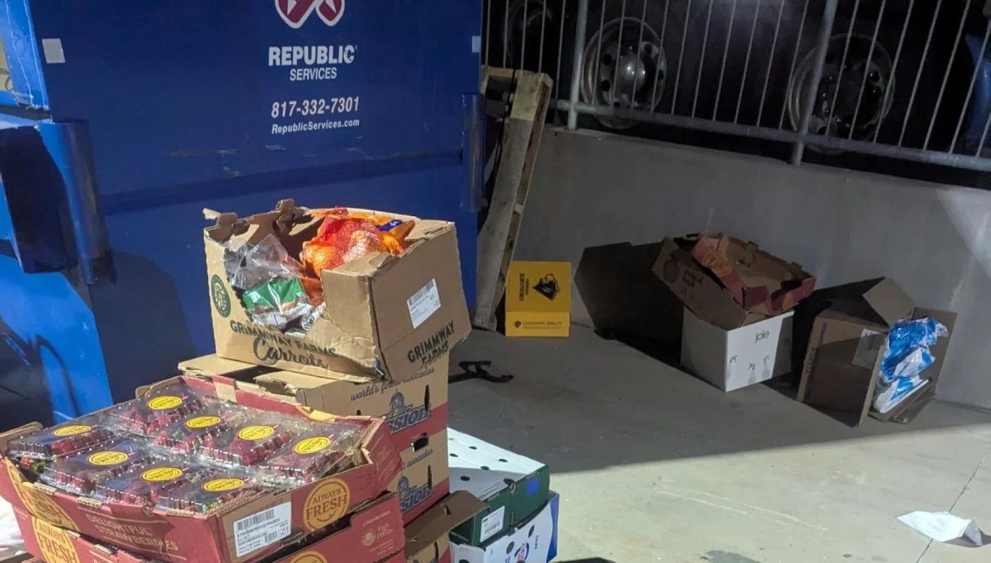 Boxes of discarded food near a dumpster.