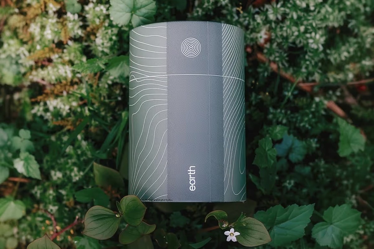 A cylindrical container with a topographical design and the word "earth" on green foliage.