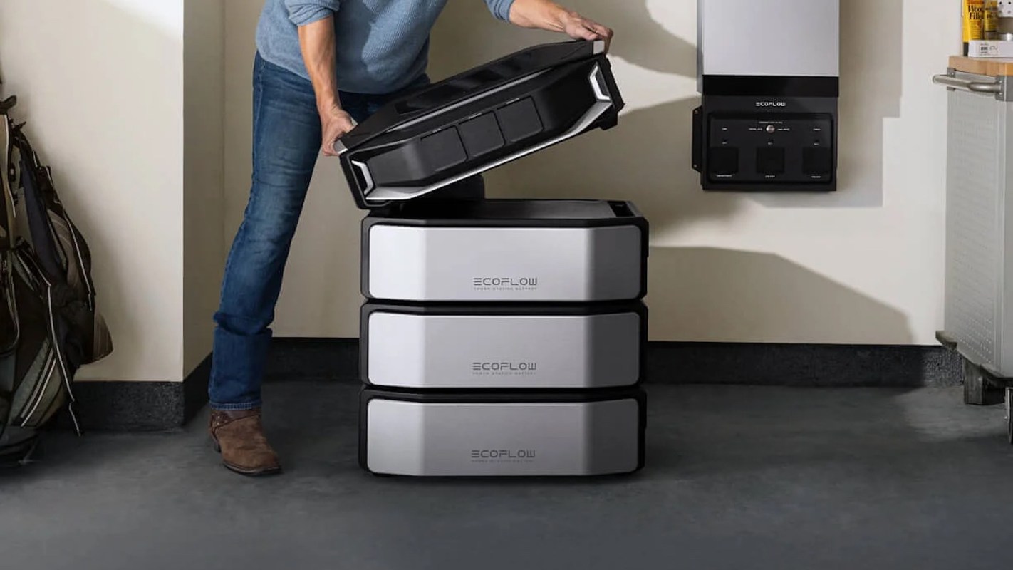 A person lifts the top storage compartment from a stack of EcoFlow modular power stations in a garage setting.