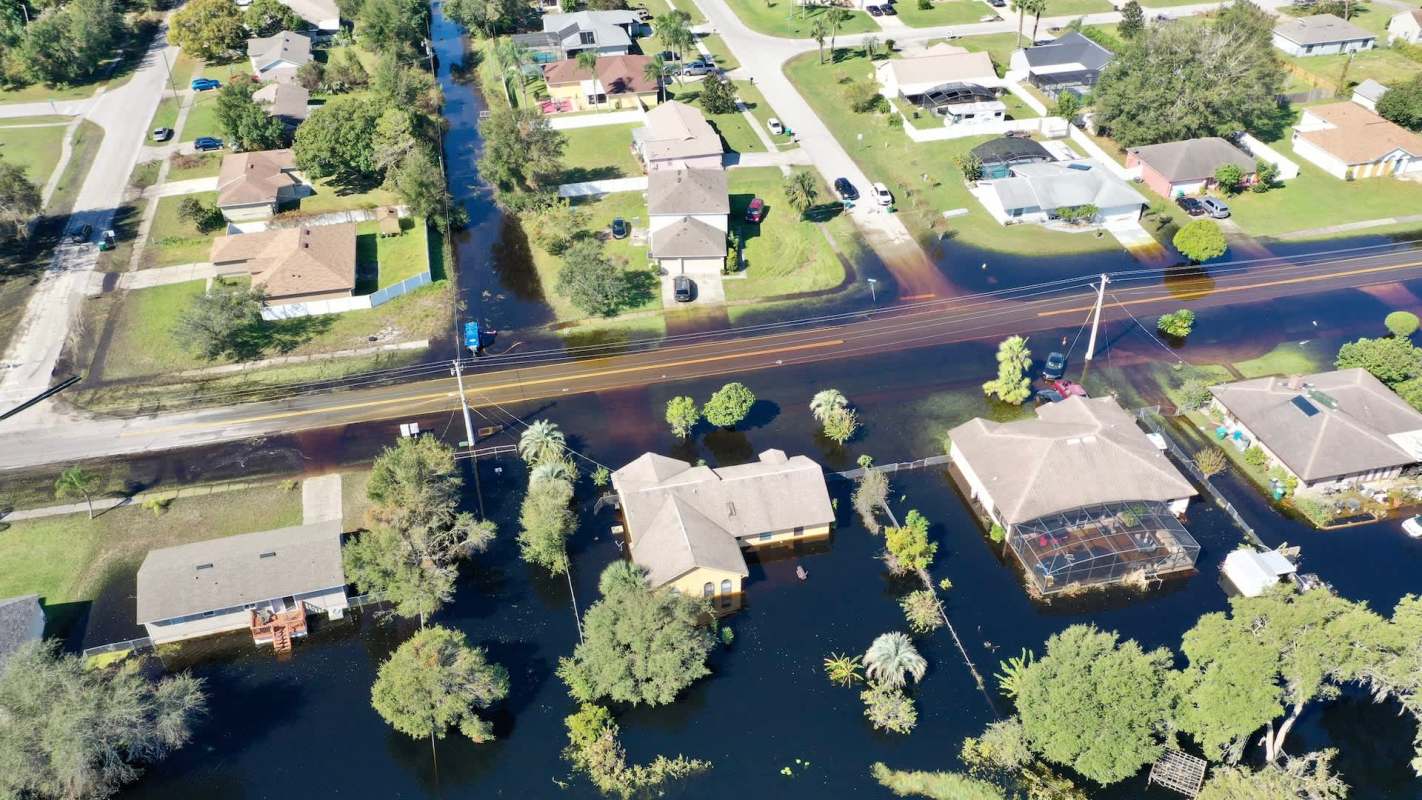 Aerial view of suburban homes partially submerged in floodwaters with streets visible in between.