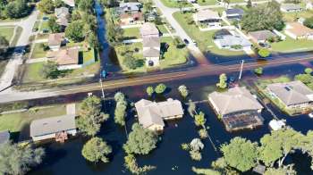 Aerial view of suburban homes partially submerged in floodwaters with streets visible in between.