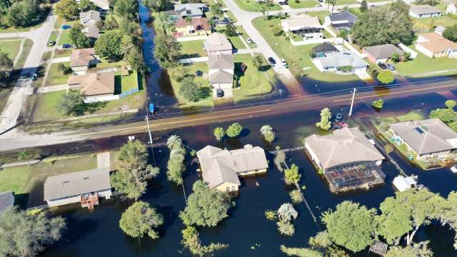 Aerial view of suburban homes partially submerged in floodwaters with streets visible in between.