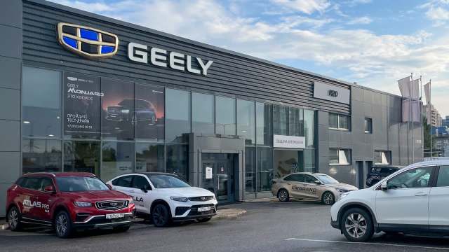 A Geely dealership with several cars parked outside and a promotional banner on the building.
