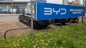 A blue sign announces the opening of a new BYD showroom, with parked cars in the background.