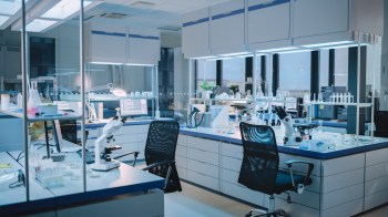 A modern laboratory equipped with microscopes, glassware, and computer workstations under bright lighting.