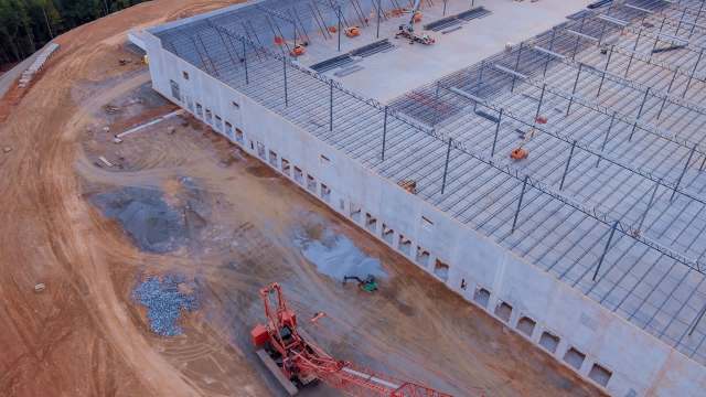 An aerial view of a data center construction site featuring a large building frame and heavy machinery on a dirt landscape.
