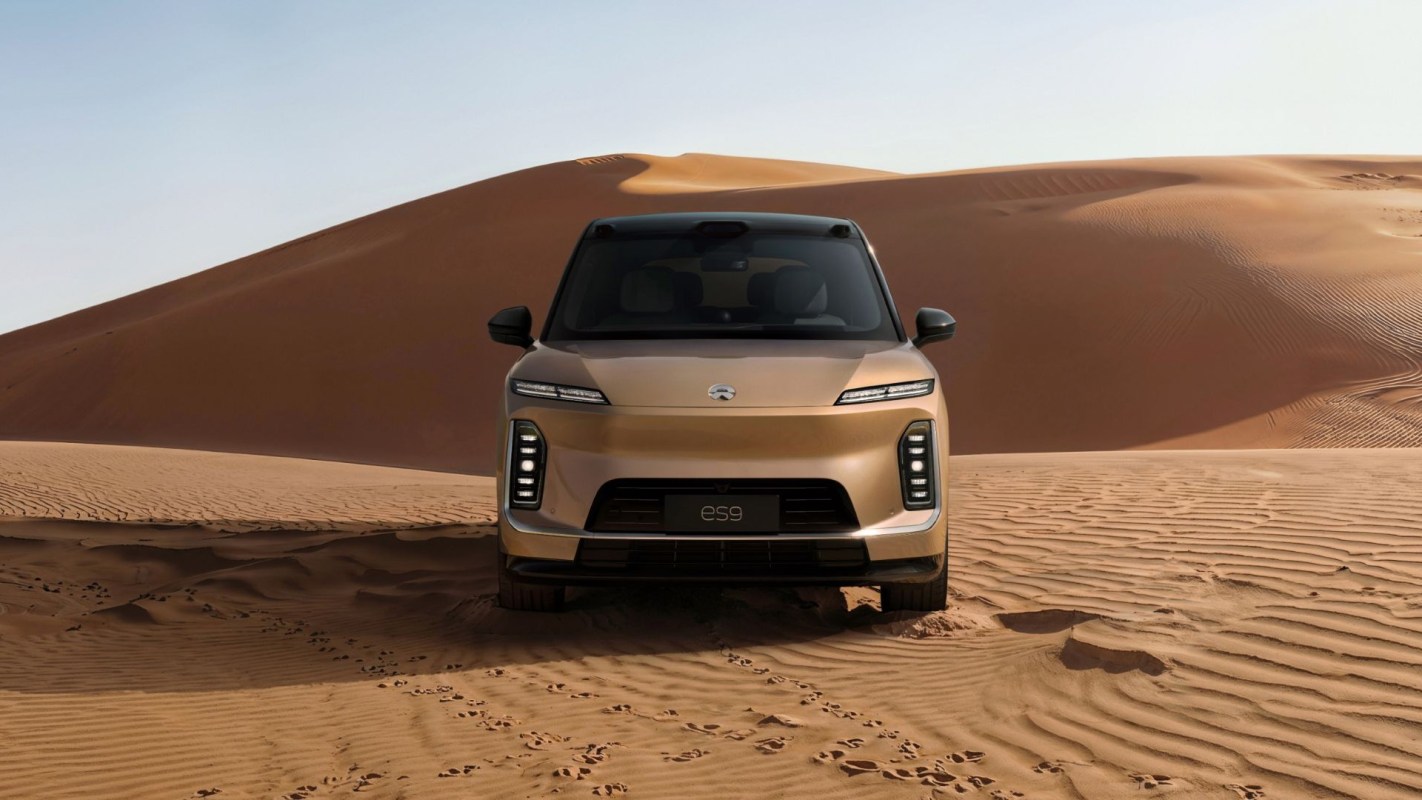 A modern SUV parked on wavy sand dunes under a clear sky in a desert landscape.