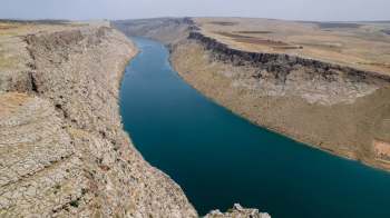A winding river flows through a rocky canyon landscape under a clear sky.