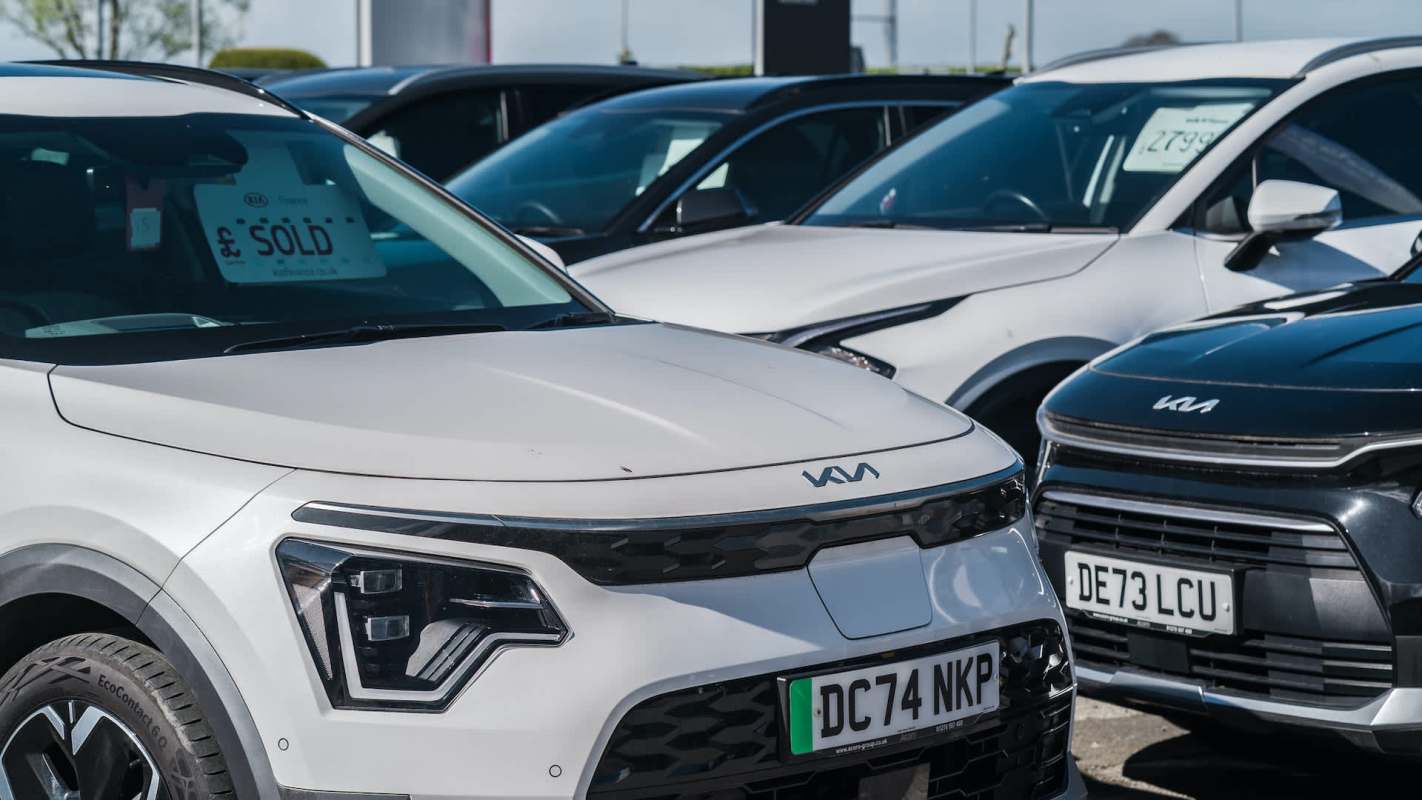 A white Kia car with a "SOLD" sign parked among other cars in a dealership lot.