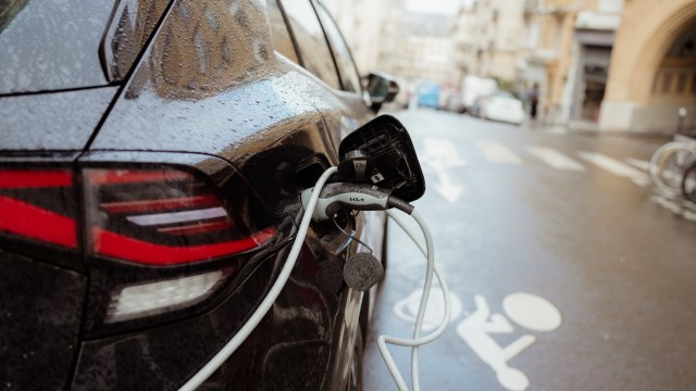 An electric vehicle parked with charging cables attached in a wet urban environment.