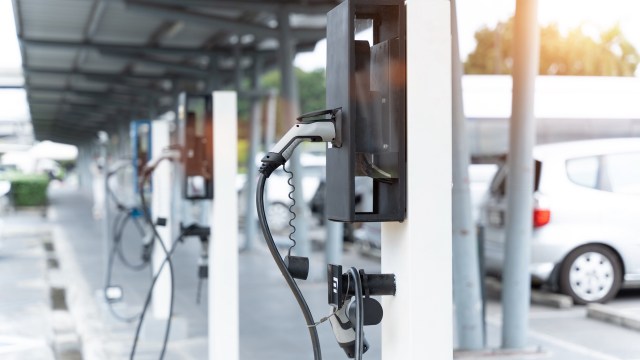 An electric vehicle charging station with a connector plugged in, surrounded by parked cars.
