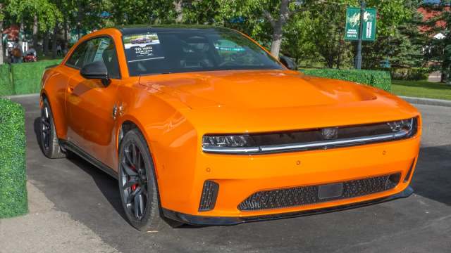 A bright orange sports car parked outside with greenery in the background.
