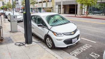 A white electric vehicle is charging at a street charging station in an urban setting.