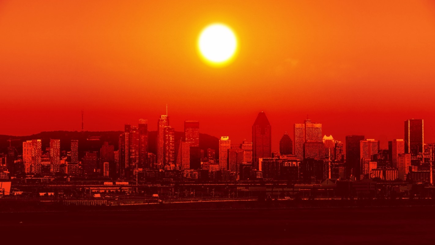 A vibrant sunset casts an orange glow over a city skyline silhouette.