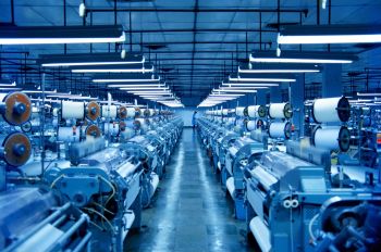 A wide view of a textile factory with rows of machinery under bright lights.