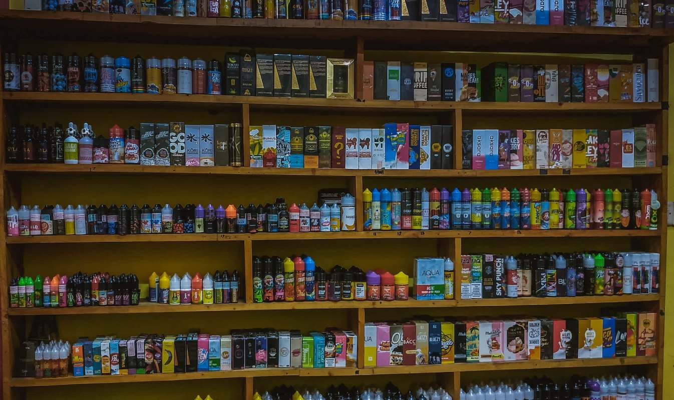 A display of various e-liquid bottles organized on wooden shelves in a vape store.