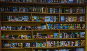 A display of various e-liquid bottles organized on wooden shelves in a vape store.