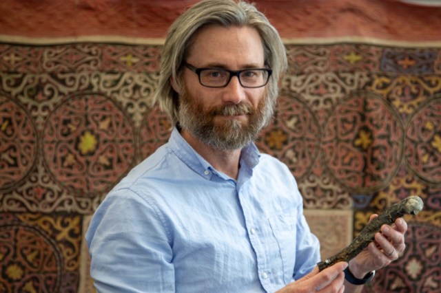 A man with glasses and a beard holds an artifact.