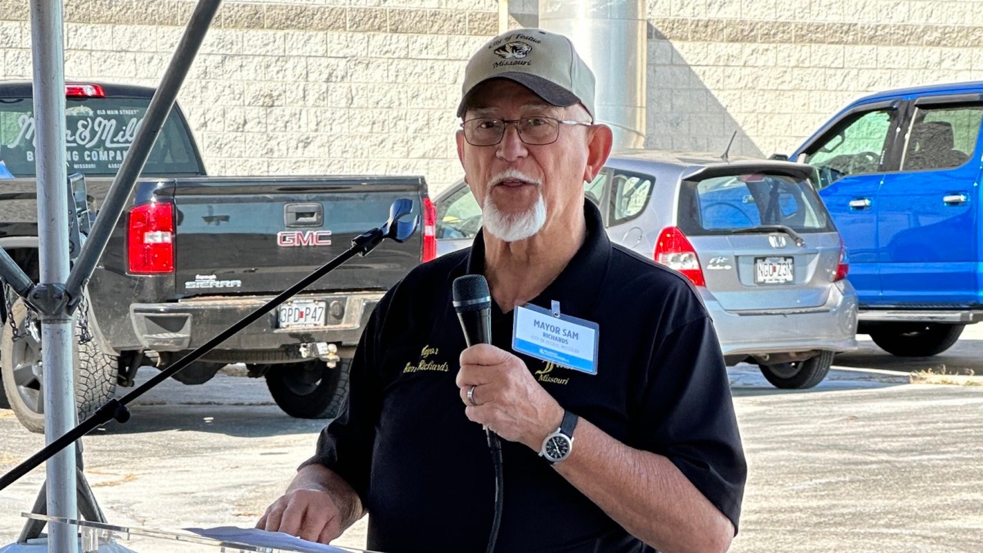 Festus mayor Sam Richards speaks at a podium under a tent, with cars in the background.