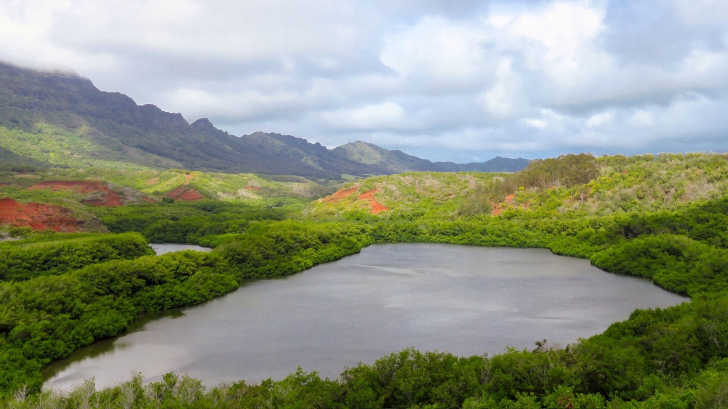 A lush green landscape surrounds a serene lake, framed by hills and cloudy skies.