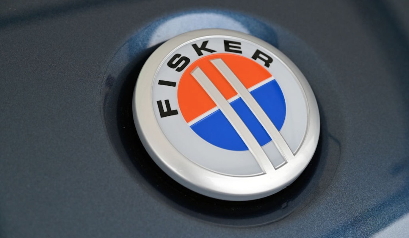 A close-up of the Fisker logo with orange and blue circular elements on a dark surface.