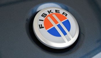 A close-up of the Fisker logo with orange and blue circular elements on a dark surface.