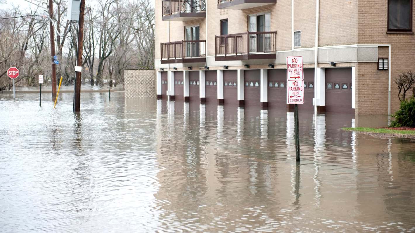 A flooded residential area with submerged garages and street signs visible amid rising water.