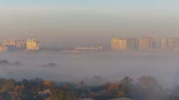 A city skyline partially obscured by morning fog, with the sun illuminating the buildings.