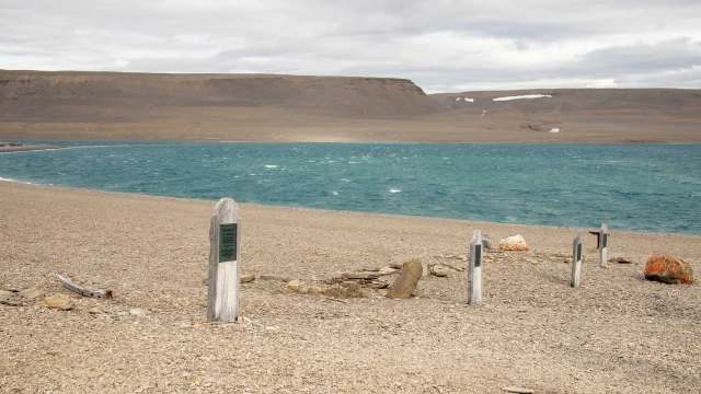A stony beach with wooden headstones and a turquoise ocean in the background under a cloudy sky.
