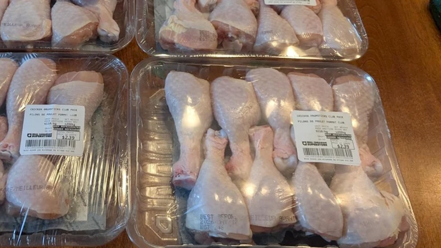 Several trays of packaged chicken drumsticks on a wooden table, labeled with prices and product information.