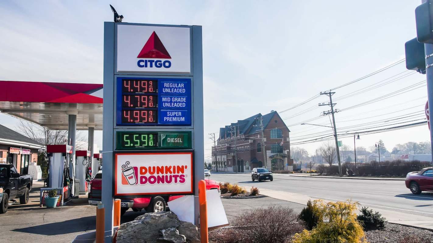 A gas station sign displaying fuel prices, including regular, mid-grade, premium, and diesel, with a Dunkin' Donuts nearby.