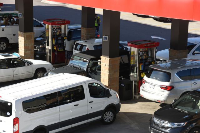 A busy gas station with multiple vehicles lined up at the fuel pumps under a large red canopy.