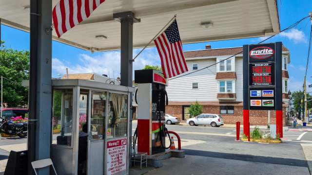 A gas station with a price display showing fuel costs and an American flag waving overhead.
