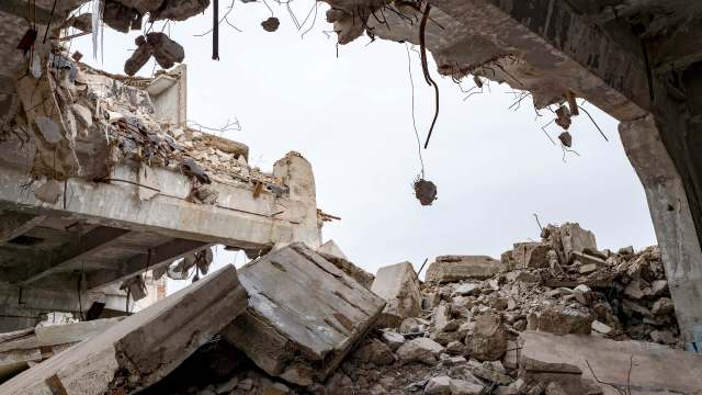 A view of a collapsed building interior, with rubble and exposed structural elements under a cloudy sky.