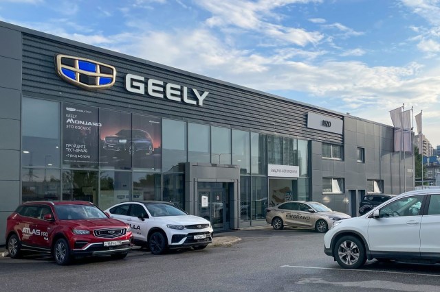 A Geely car dealership showcasing several parked vehicles and large windows displaying promotional signage.