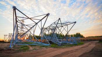 A partially constructed electrical transmission tower against a colorful sunset and a grassy field.