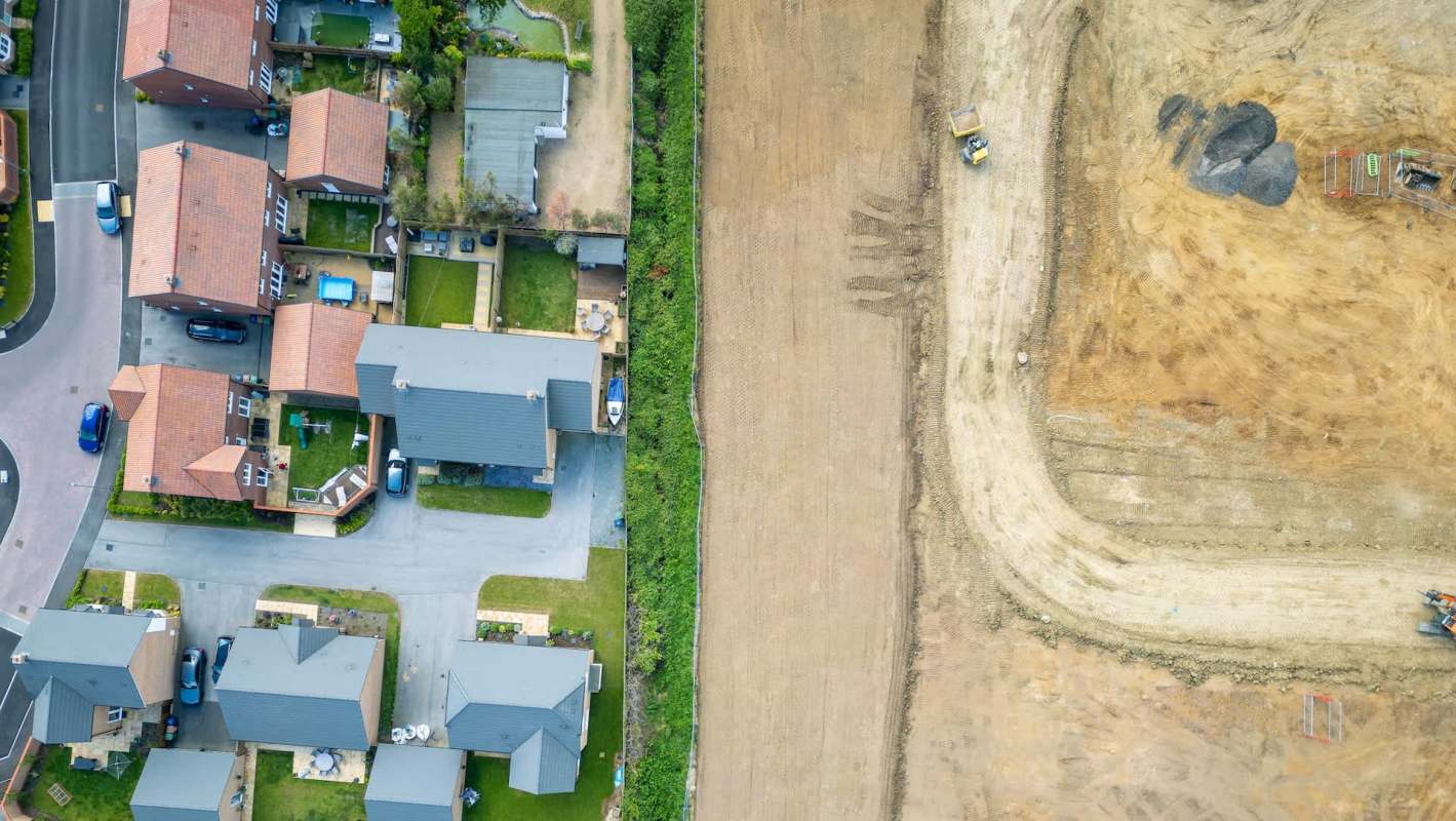 Aerial view of suburban houses next to a large cleared field with construction equipment nearby.