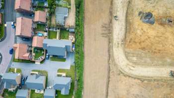 Aerial view of suburban houses next to a large cleared field with construction equipment nearby.