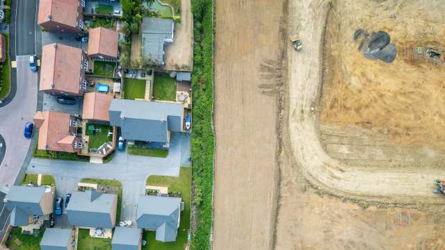 Aerial view of suburban houses next to a large cleared field with construction equipment nearby.