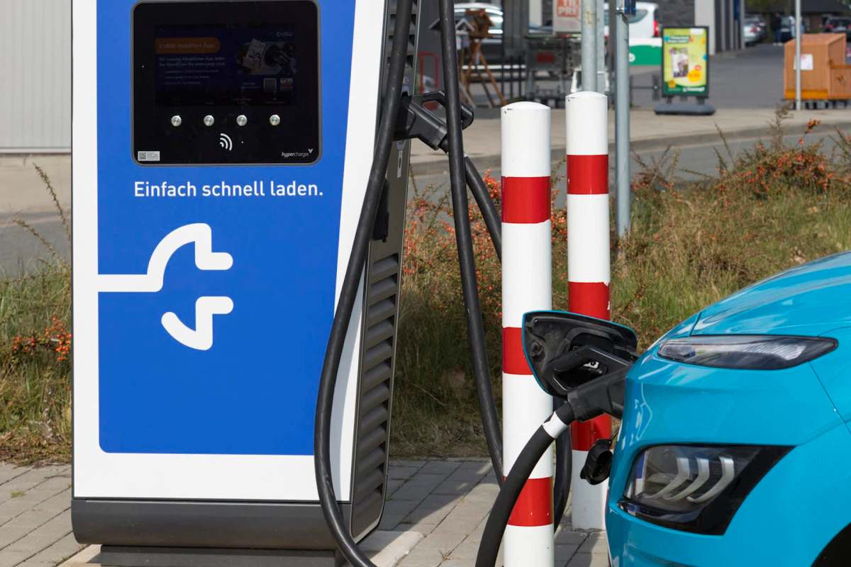 An electric vehicle charging at a station by white and red striped posts.