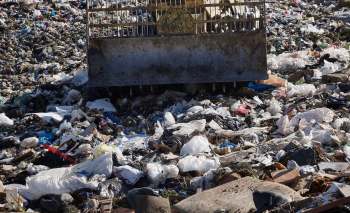 A landscape covered in a large amount of litter and waste, with a bulldozer in the background.