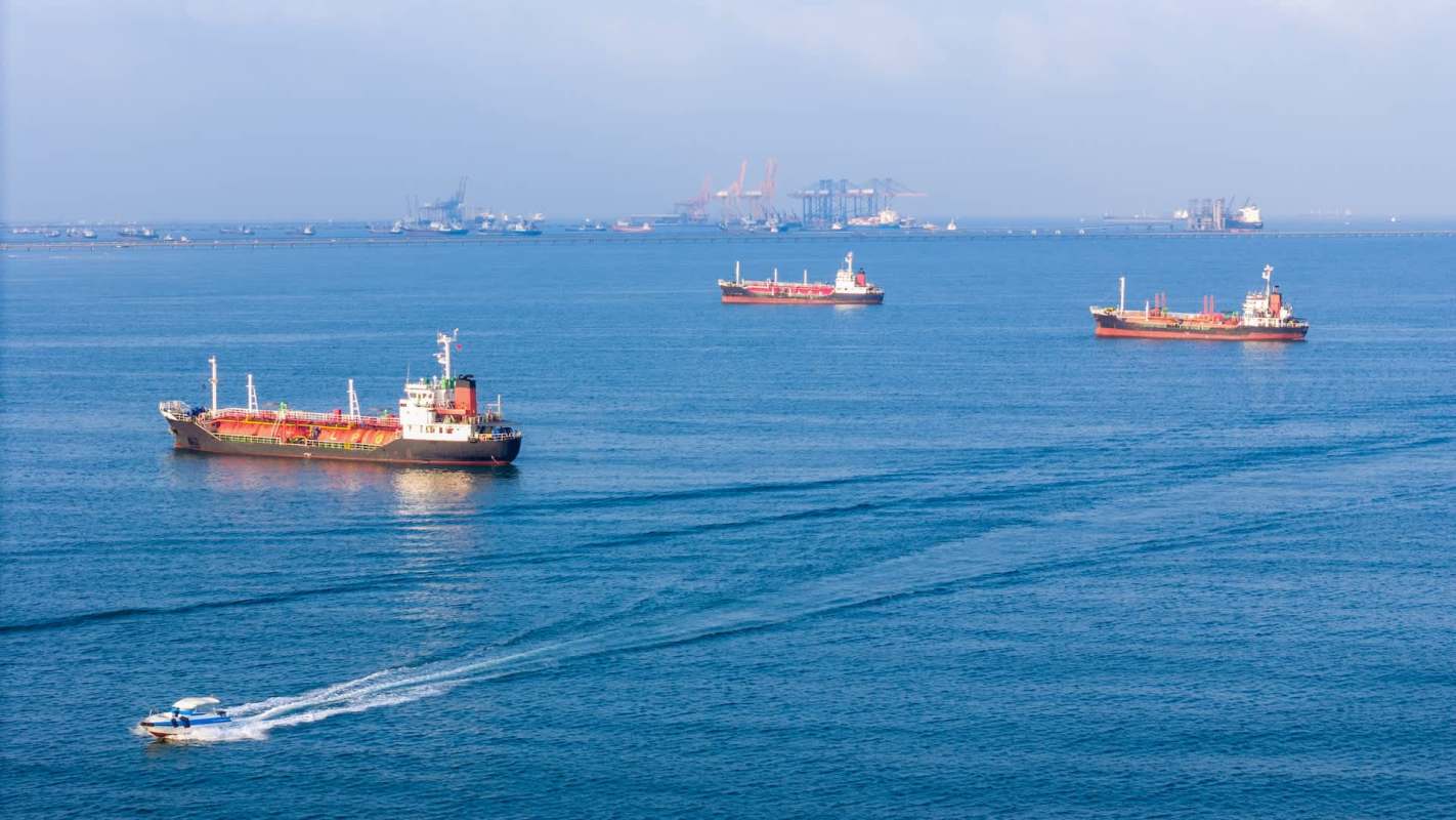 Several cargo ships and a smaller boat navigate a calm sea under a clear sky.