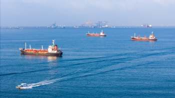 Several cargo ships and a smaller boat navigate a calm sea under a clear sky.