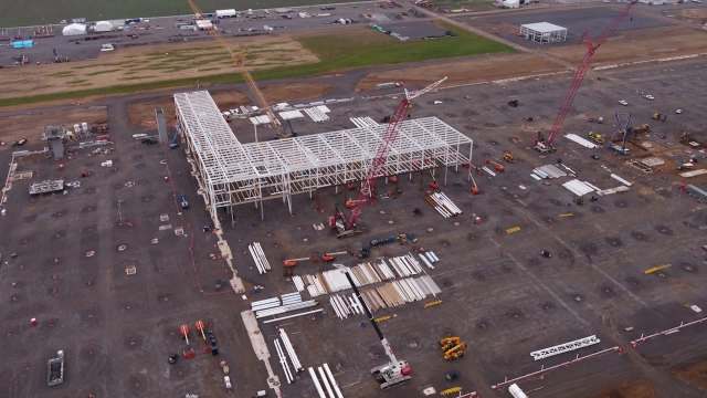 Aerial view of a construction site with cranes, machinery, and structural frames in progress.